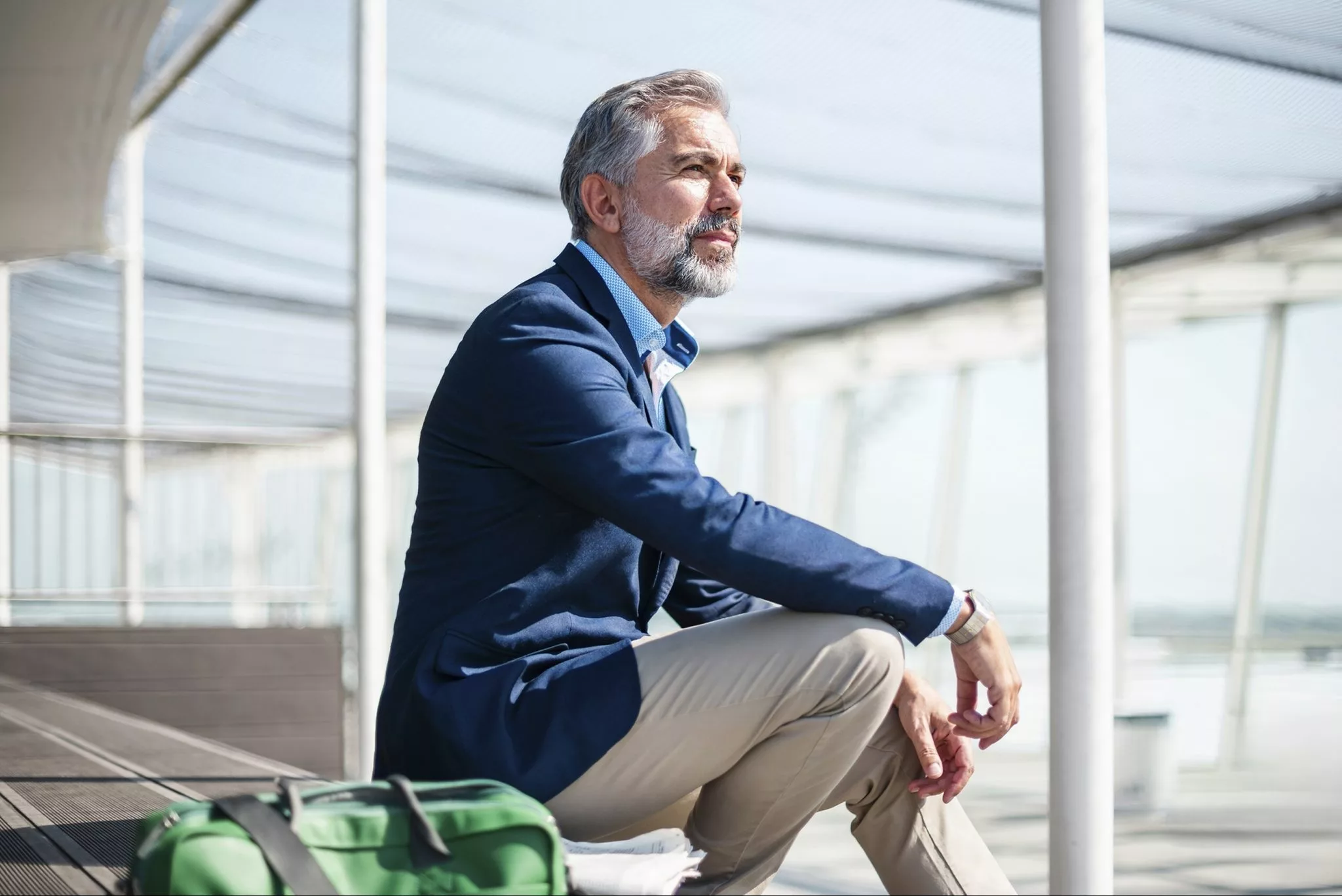 Older man sitting on a bench in a bright airport terminal, representing the freedom a secure financial future makes possible.