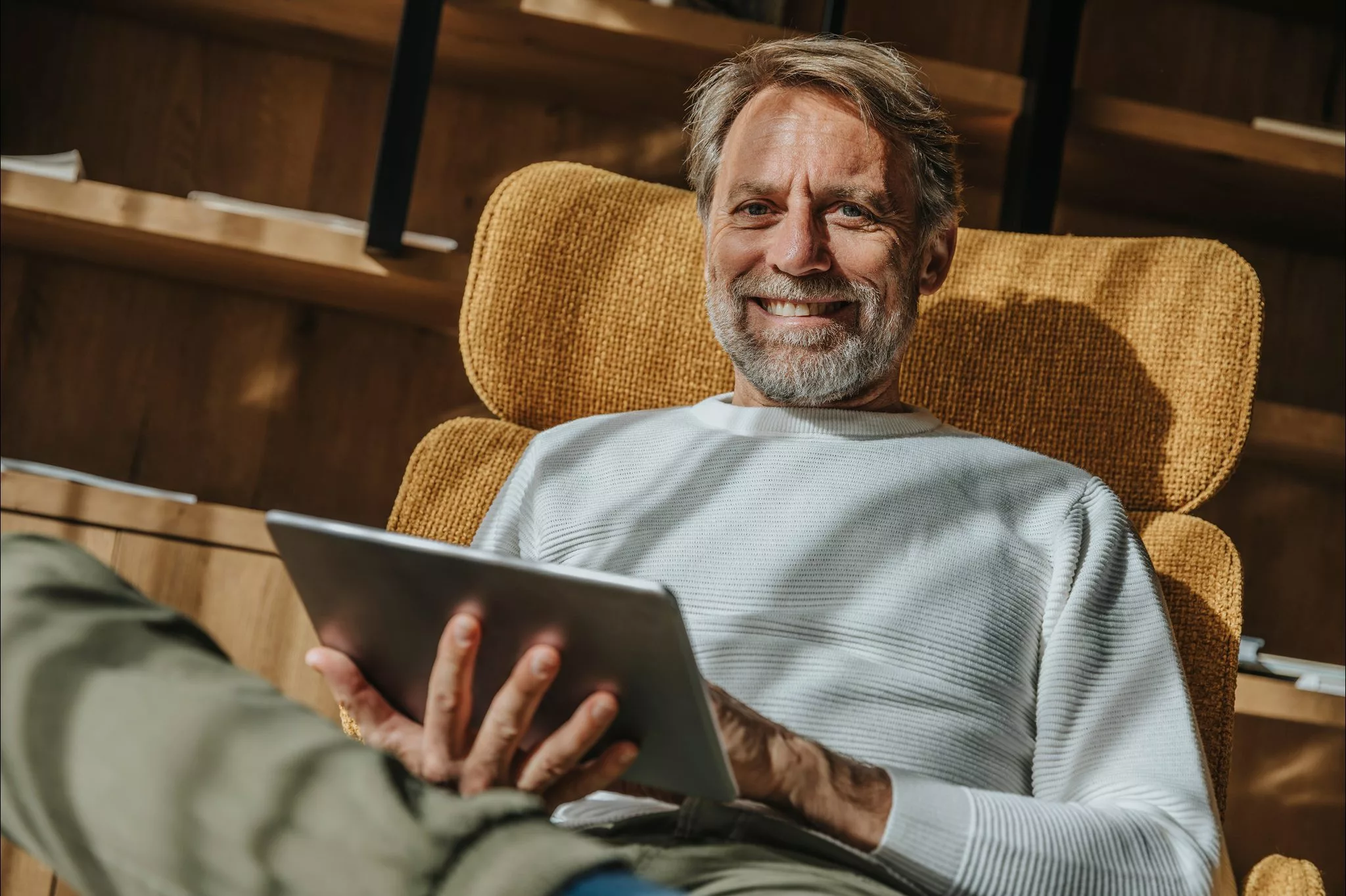 Man relaxing at home while using a tablet, reflecting the ease a trusted wealth management partner provides.