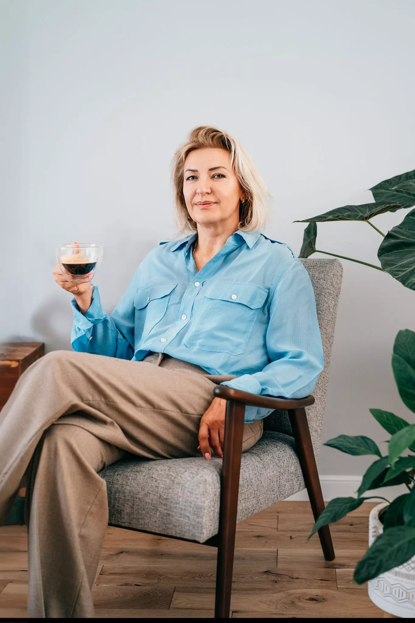 Woman relaxing in a modern armchair with coffee, reflecting the peace of mind sound wealth management brings.
